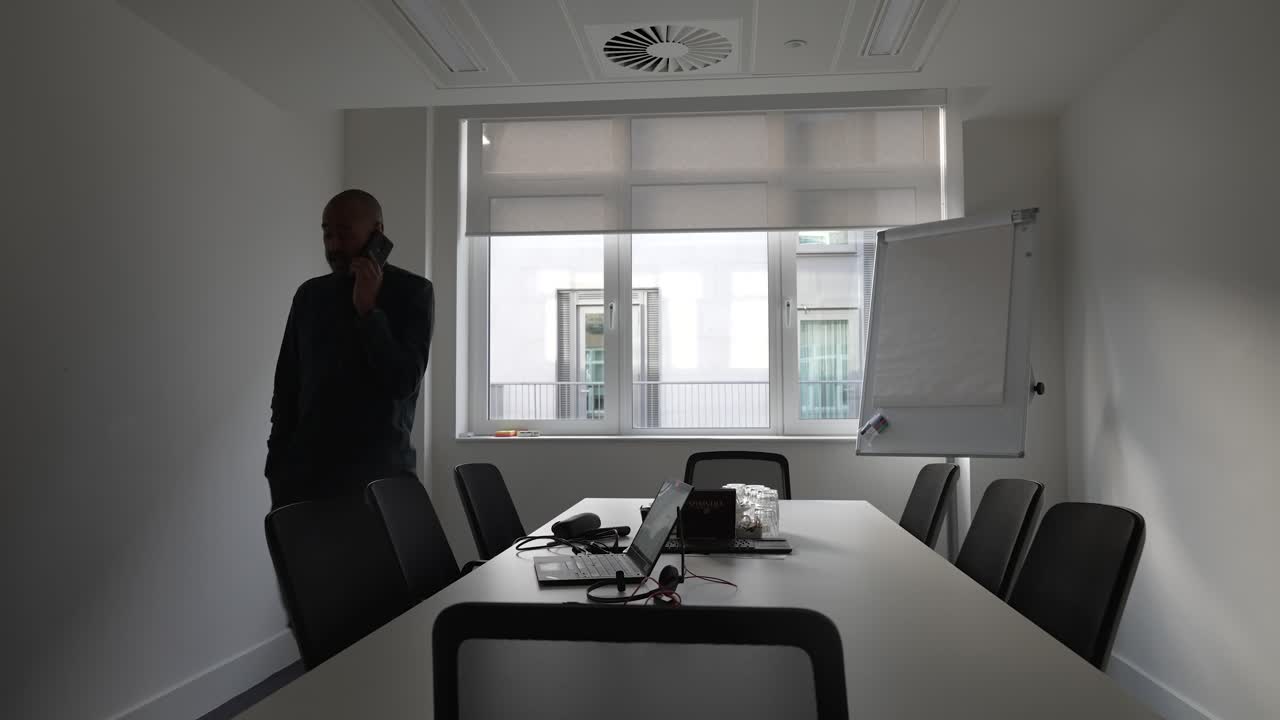 Imprenditore calvo che parla al cellulare camminando avanti e indietro nella sala riunioni dell'ufficio