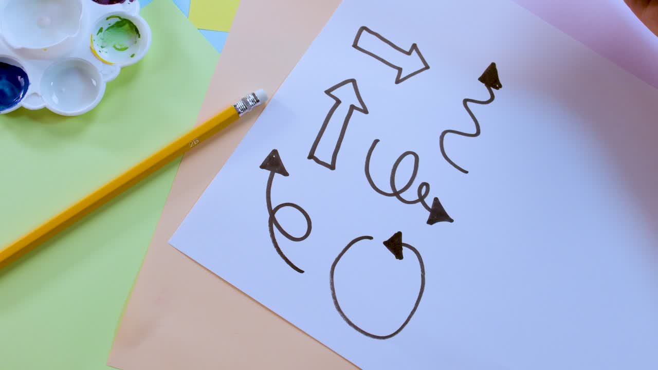 Overhead view of person drawing arrows and curly lines on paper with black marker