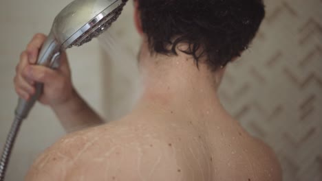 white man with dark hair washes his neck with the shower head in his hand