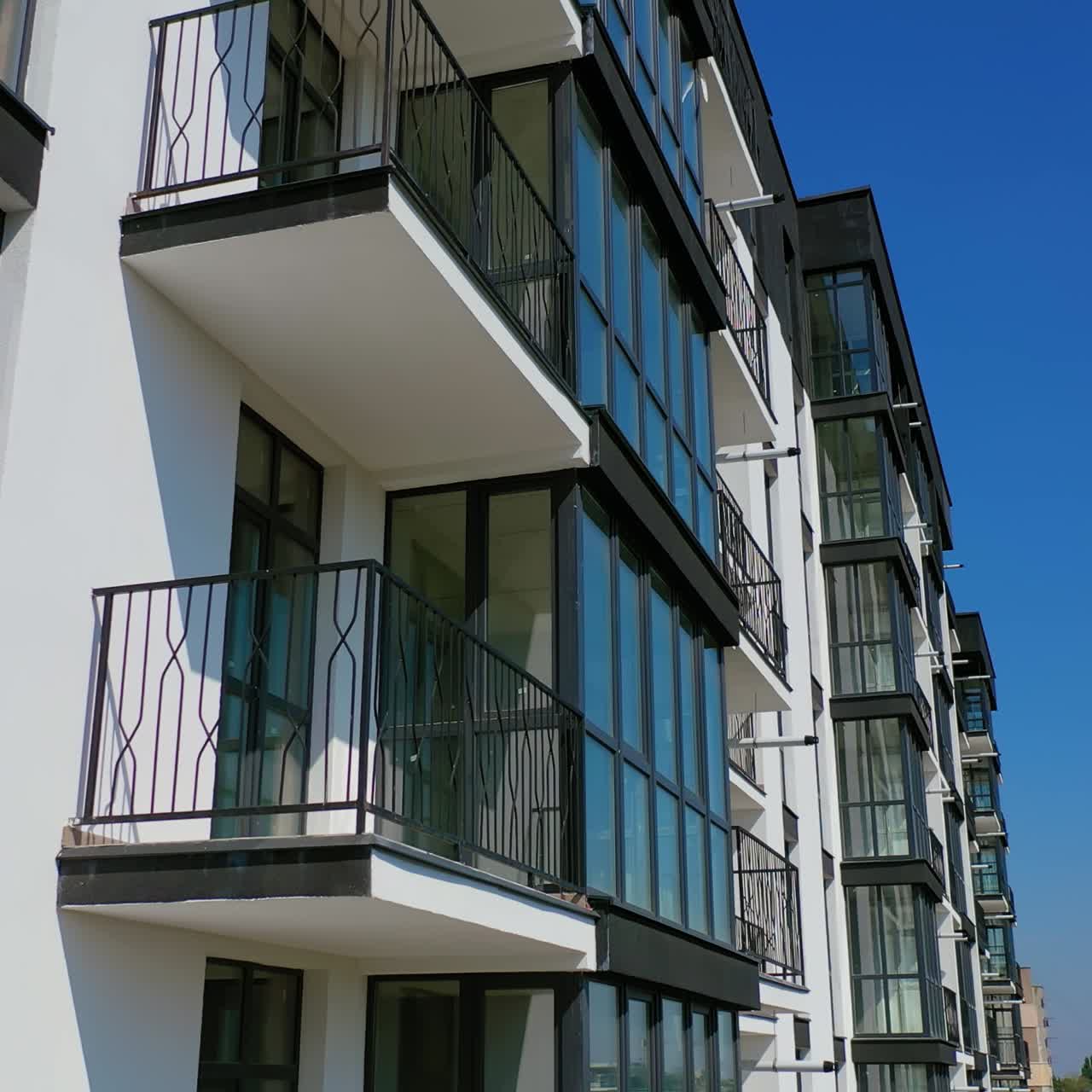 Beautiful design of multistorey building. New apartment with balconies against blue sky. Exterior of residential building. Camera rising up. Slow motion.