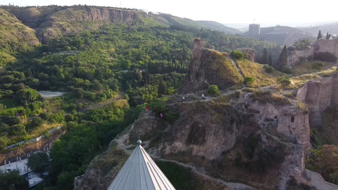 toma cinematográfica de drones que muestra colinas y revela una hermosa iglesia amarilla durante un día soleado en tblisi