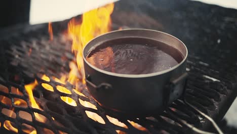 Boiling-hot-glogg-on-a-grill-over-campfire-in-woods-in-winter-in-Lemmenlaakso,-Finland