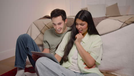 pareja viendo una película interesante en una tableta mientras se sienta en el suelo en casa 2