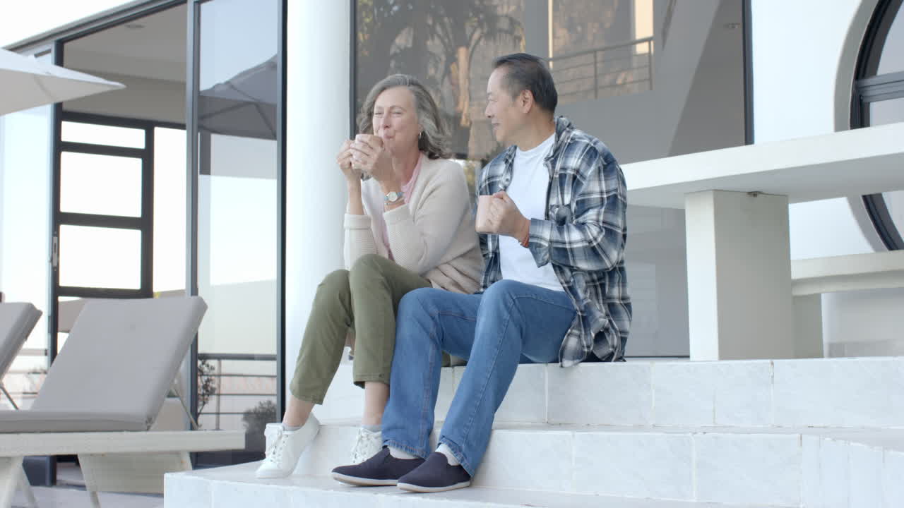 Senior couple sitting on steps, enjoying coffee and conversation outdoors