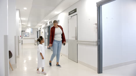 african american mother and daughter in hospital gown holding hands walking in corridor, slow motion
