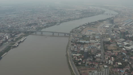 Langsamer-Luftschwenk-über-Phnom-Penh-Und-Tonle-Saugt-Seine-Brücke-An-Einem-Verschmutzten-Tag-Ab