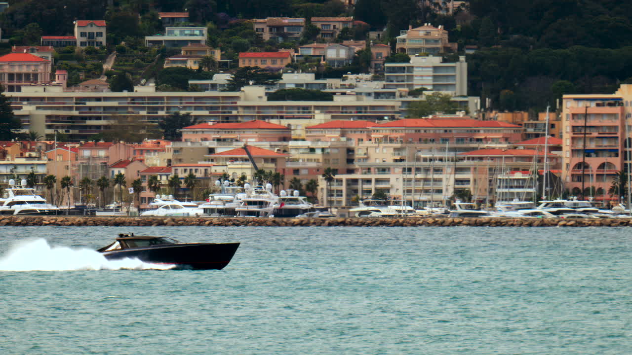 Boat moving on the sea in Juan-les-Pins, France with the dock and the buildings on the background