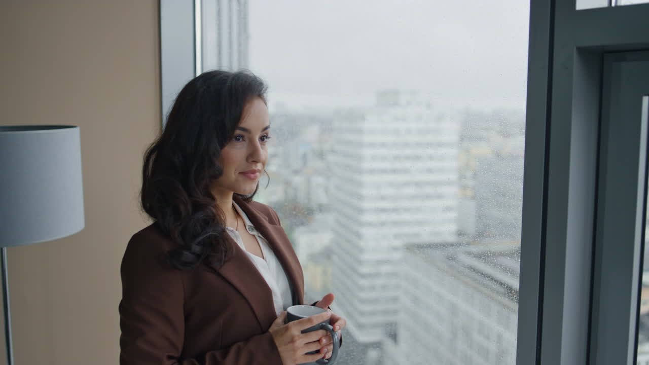mujer de negocios bebiendo café en la oficina mirando la ventana panorámica de cerca.