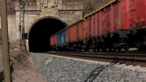 cargo train with lorries drives into pitch black tunnel, static railway shot