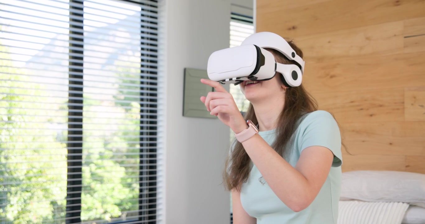 Donna che allunga la mano per prendere un visore VR bianco vicino al telefono sul letto, regolandolo e selezionando menu virtuali.
