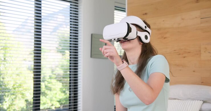Donna che allunga la mano per prendere un visore VR bianco vicino al telefono sul letto, regolandolo e selezionando menu virtuali.