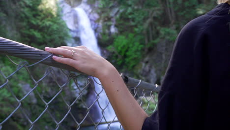 Woman-crossing-old-traditional-bridge-in-forest-in-British-Columbia-BC,-Canada-with-waterfall-and-river-and-hand