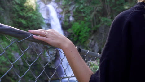 mujer cruzando el viejo puente tradicional en el bosque en columbia británica bc, canadá con cascada y río y mano
