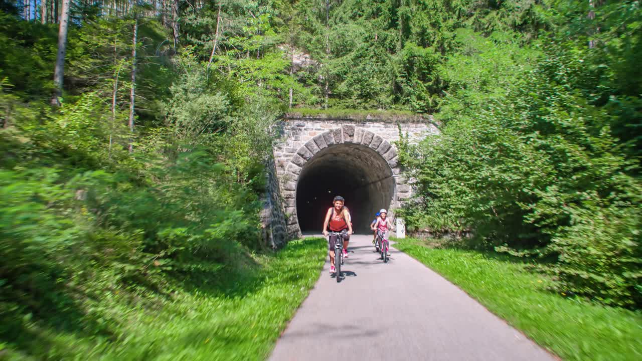 Lifestyle family of four cycling out forest tunnel in Slovenia, tilt down