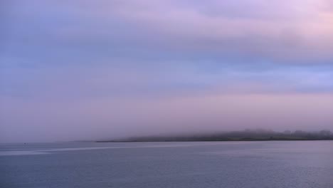 niebla sobre el mar y la ciudad costera al amanecer con aguas tranquilas y cielo colorido