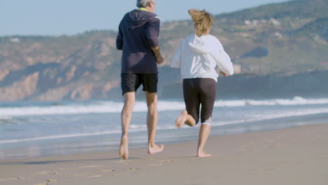 elderly couple running barefoot on sandy beach and having fun