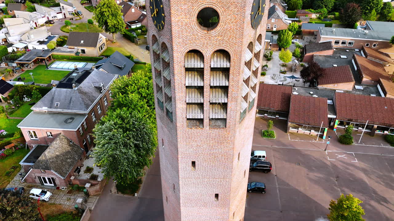 Rise along the brick tower with clock. Church in Vierlingsbeek, Netherlands. Green residential area at backdrop