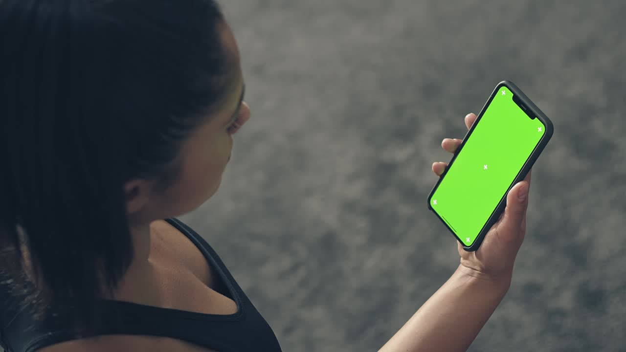 vista trasera de fitness mujer usando teléfono inteligente de pantalla verde en casa. mujer preparándose para el entrenamiento usando teléfono inteligente. mujer usando teléfono móvil mientras descansa durante el entrenamiento de fitness