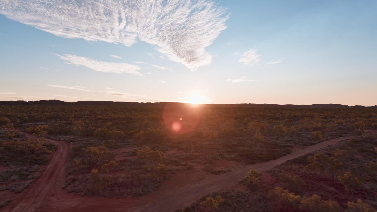 pista izquierda, camino de tierra del interior rojo sucio de australia con el sol poniéndose, cielo azul con algunas nubes, monte isa, queensland, australia