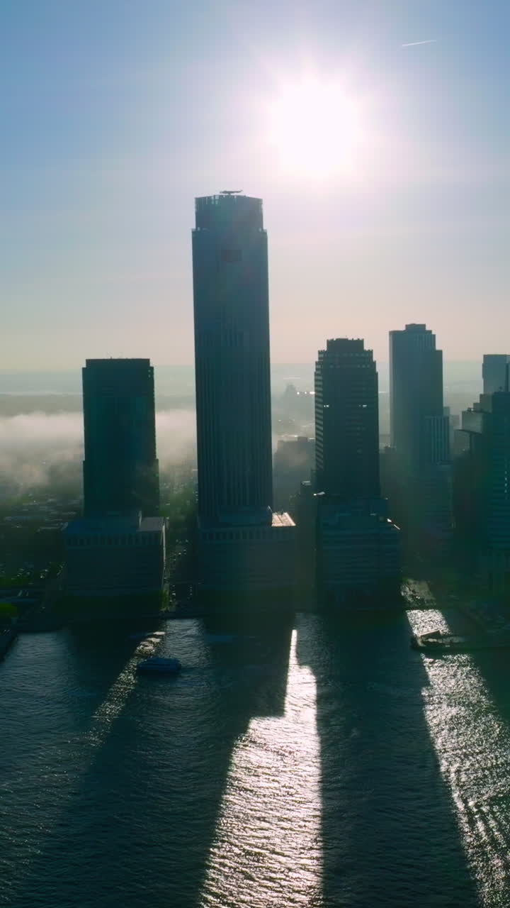 Grey silhouettes of New York skyscrapers against the sun. Rays are coming between the buildings. Fog spreading on the city. Vertical video