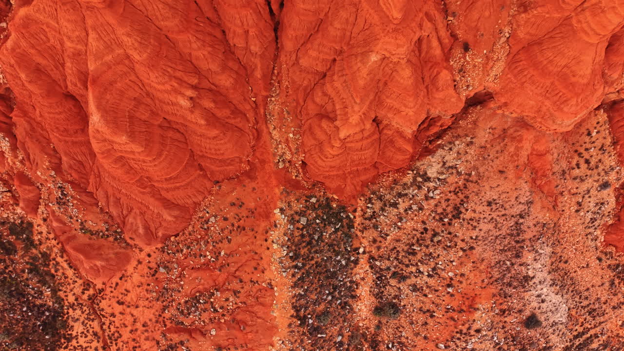 Vista aerea dall'alto di terreno argilloso rosso eroso. Scatto verticale di roccia sedimentaria rossa e terreno arido con vegetazione rada.