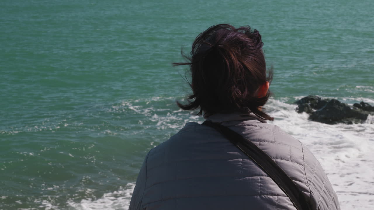 Close up over the shoulder of an attractive woman relaxing and looking at the ocean on vacation, Greystones, Ireland