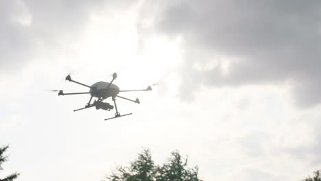 handheld camera tracks a white drone with six propellers, flying towards the right in a cloudy sky with the sun peeping through