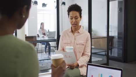 Two-happy-diverse-businesswomen-with-coffee-working-together-in-office