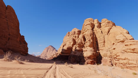 tire tracks in desert sand lead to massive sandstone towers in wadi rum