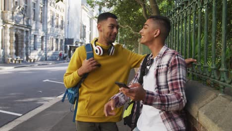 two happy mixed race male friends standing and using smartphone in the street