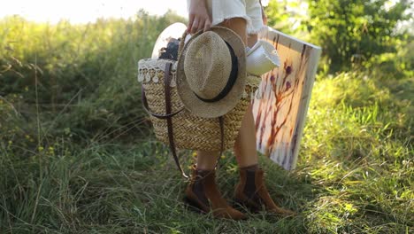 woman carrying a basket with a hat and a painting in a field