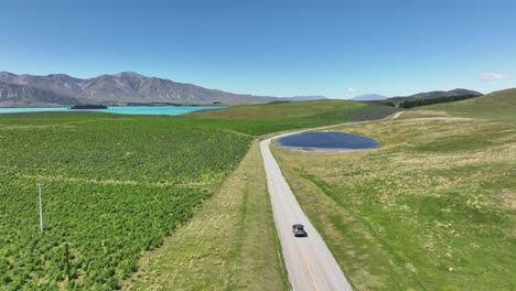 Car-travels-on-dirt-road-going-to-Lake-Tekapo-on-summer-day,-aerial