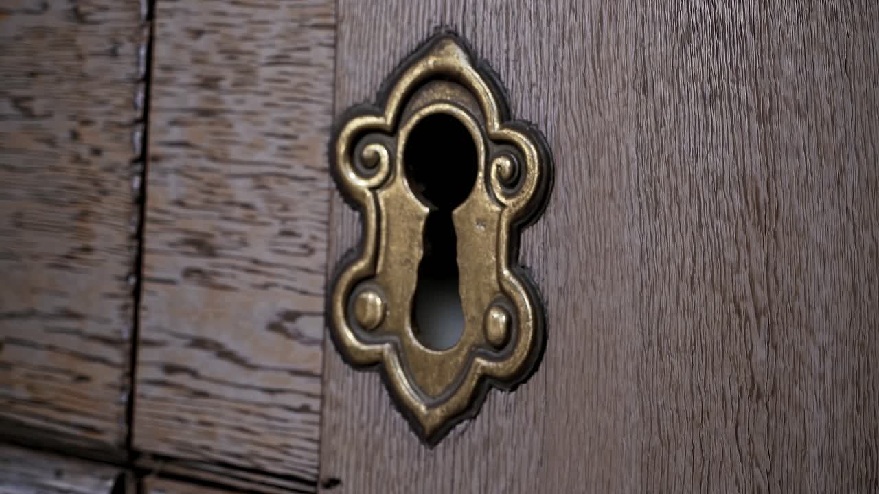 Close-up video of an ornate brass keyhole on a rustic wooden door, shot from a side angle