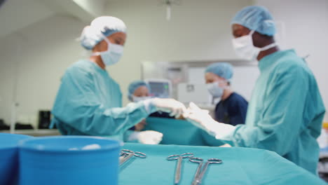 nurse hands surgeon medical instruments as surgical team work on patient in operating theatre