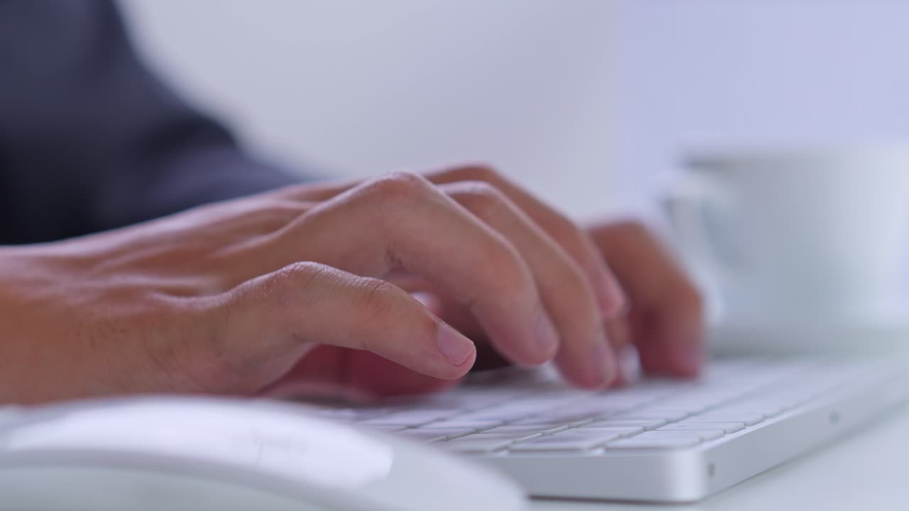 Side angle of businessman hands typing on wireless keyboard at professional desk with coffee cup