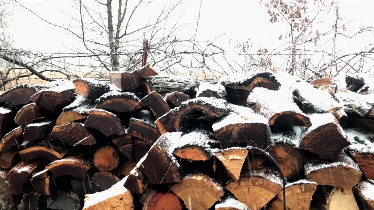 Left to right pan of a stacked wood pile while snowing.