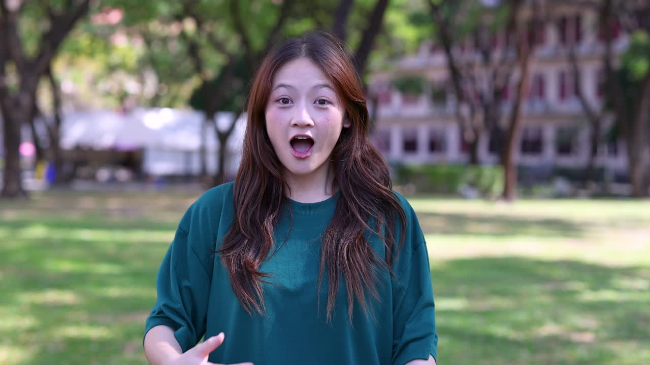 晴れた屋外の公園で、胸に手を当てて息をのむ、ショックを受けた若い女性