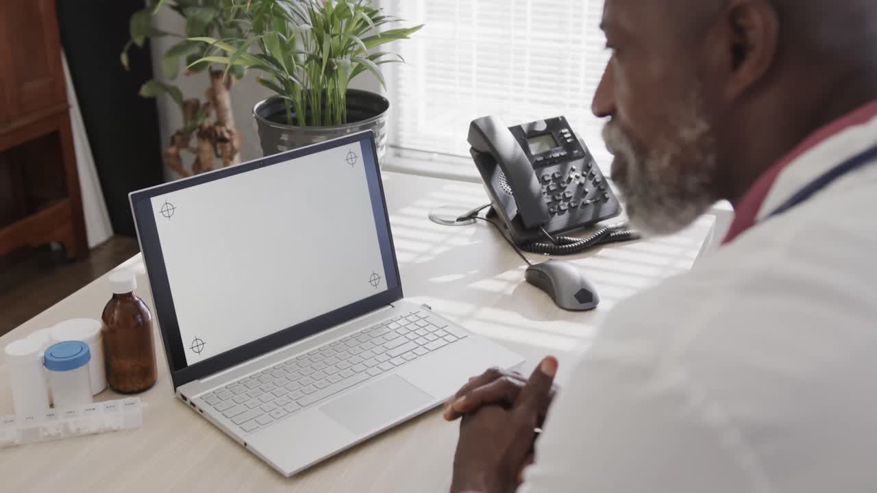 médico afroamericano sentado en un escritorio y usando una computadora portátil con espacio para copiar, cámara lenta