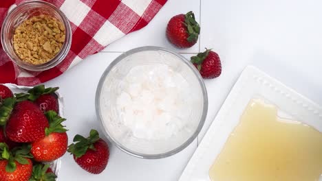 making a strawberry shortcake martini and adding in the vanilla vodka with the other ingredients. strawberries on a red and white gingham napkin. close up of making a cocktail martini for happy hour