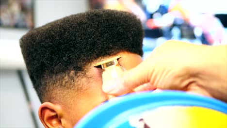 primer plano estático de peluquero haciendo corte de pelo en línea en un niño afroamericano con recortadores o cortapelos inalámbricos dorados