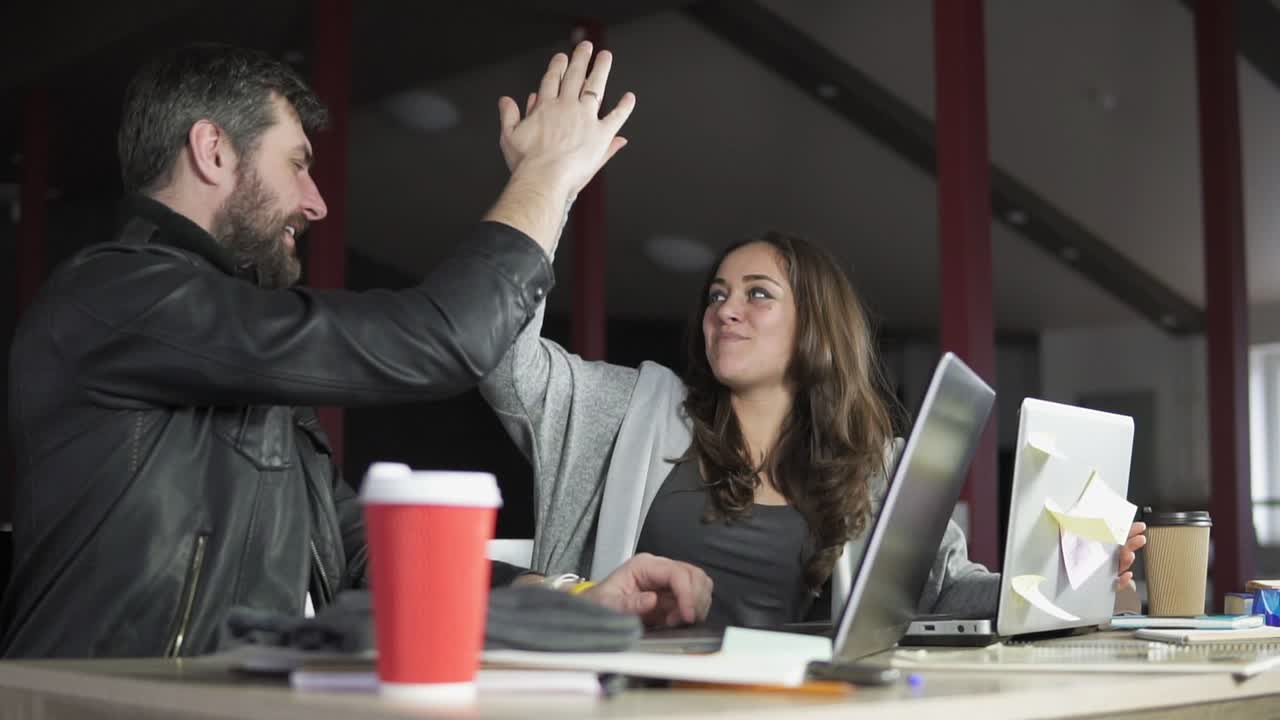 hombre y mujer jóvenes están trabajando juntos frente a sus computadoras portátiles, sentados juntos en la mesa.