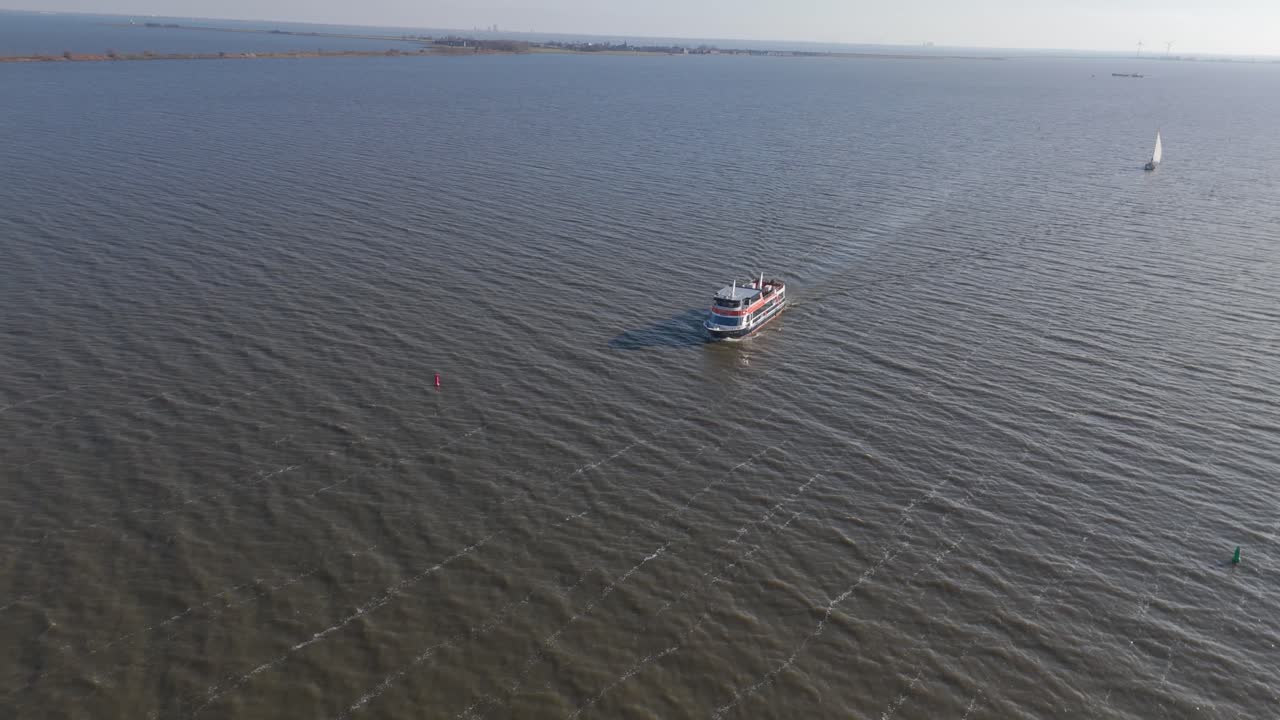 Riprese aeree con drone di una barca turistica che naviga sul Markermeer vicino a Volendam, Paesi Bassi, con acqua calma e la suggestiva costa olandese