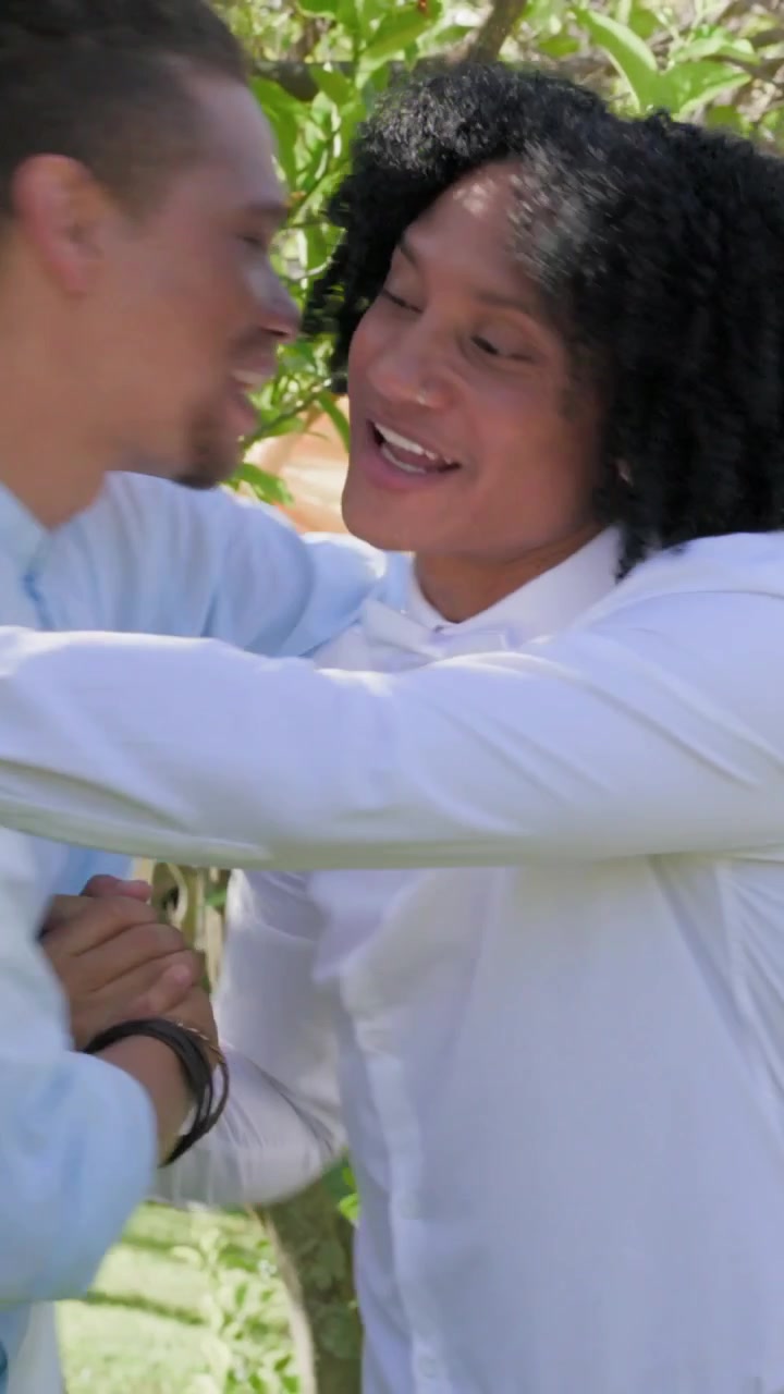 Video verticale: Uomo in camicia bianca che inizia a salutare gli ospiti abbracciandoli all'arco con la boutonnière.
