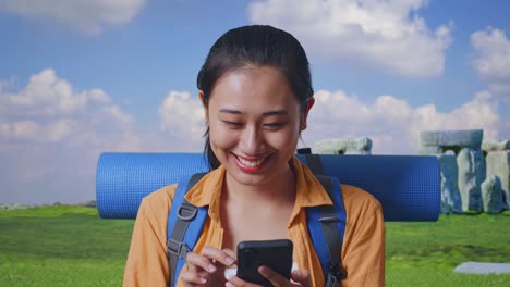 Close Up Of Asian Female Hiker With Mountaineering Backpack Enjoy Using Smartphone While Traveling In Stonehenge
