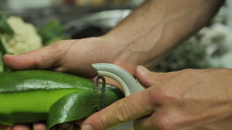 Unrecognizable-chef-peeling-avocado-on-vegetable-background,-close-up-on-hands