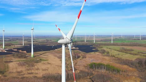 Drone-shot-of-large-power-plant-of-solar-panels-in-Electrum-solar-park-and-wind-turbines-in-a-vast-field-on-a-sunny-day-in-Taurage,-Lithuania