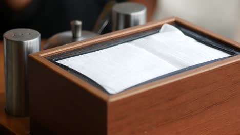 close-up of a hand reaching for a napkin in a wooden holder