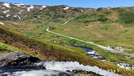 norewgian mountain road rv 13 seen from a distance in idyllic surroundings with river stream passing close to camera - static handheld clip from vikafjell norway