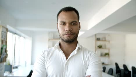 Young-bearded-guy-standing-with-crossed-arms-at-office.