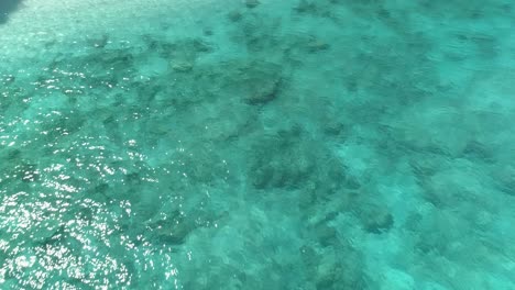 revealing three people stranded - lost at a loneley beach with caribbean look, rocks, turqouise water, mountains and white beach - aerial establishing drone shot